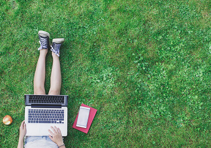 Top view image of young girl sitting in grass with her laptop and smartphone. Web design template with copy space.